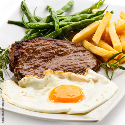 Photo: Grilled steaks, French fries, fried egg and vegetables Grilled steaks, French fries, fried egg and vegetables