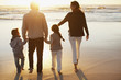 Family holding hands and walking on beach at sunset