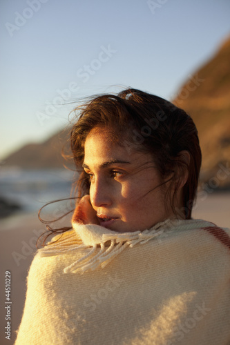 Photo: Pensive woman wrapped in blanket on beach Pensive woman wrapped in blanket on beach