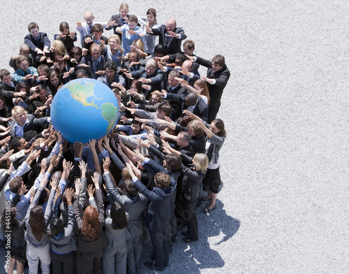 Photo: Crowd of business people in huddle reaching for globe Crowd of business people in huddle reaching for globe