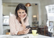 Smiling businesswoman looking down at cell phone in cafe window