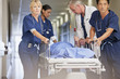 Doctor and nurses wheeling patient in gurney down hospital corridor
