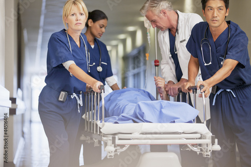Photo: Doctor and nurses wheeling patient in gurney down hospital corridor Doctor and nurses wheeling patient in gurney down hospital corridor
