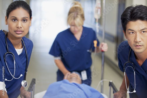 Photo: Nurses wheeling patient on gurney down hospital corridor Nurses wheeling patient on gurney down hospital corridor