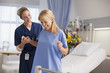 Nurse helping happy patient stand in hospital room
