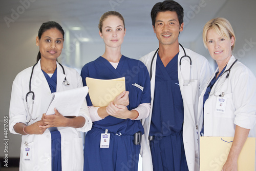 Photo: Portrait of smiling doctors and nurse holding medical records in hospital corridor Portrait of smiling doctors and nurse holding medical records in hospital corridor
