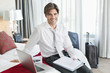 Portrait of smiling businessman with paperwork and laptop on bed in hotel room