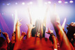 Stage lights shining on audience with arms raised at music concert