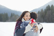 Smiling woman holding Christmas gift and hugging man in snow