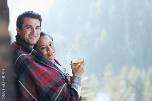 Photo: Portrait of smiling couple wrapped in a blanket and drinking hot cider on porch Portrait of smiling couple wrapped in a blanket and drinking hot cider on porch