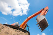 Excavator standing in a ground with raised bucket over sky