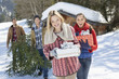 Portrait of smiling couples with fresh cut Christmas tree and gifts in snow