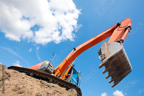 Photo: Excavator standing in a ground with raised bucket over sky Excavator standing in a ground with raised bucket over sky