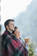 Smiling couple wrapped in a blanket and drinking tea outdoors