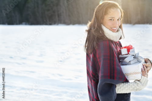 Photo: Portrait of smiling woman carrying Christmas gifts in snow Portrait of smiling woman carrying Christmas gifts in snow