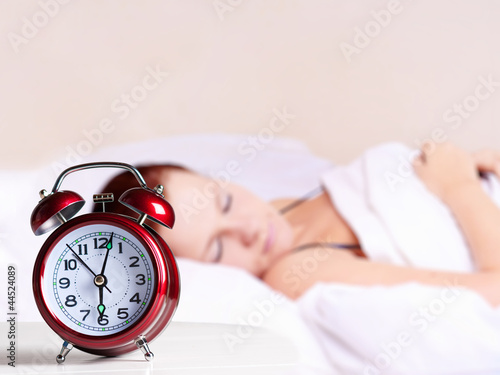 Foto: Young sleeping woman and alarm clock in bedroom at home. Young sleeping woman and alarm clock in bedroom at home.