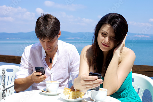 Photo: Couple texting having breakfast in front of lake Couple texting having breakfast in front of lake