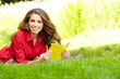 Young beautiful woman lays on green field and reads book.