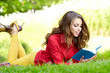 Young beautiful woman lays on green field and reads book.