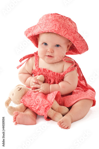 Photo: Smiling baby girl in pink dress and sun hat sits and plays with Smiling baby girl in pink dress and sun hat sits and plays with