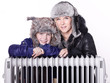 Mother and daughter in warm winter coats leaning over a radiator