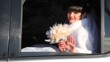 bride and with bouquet of roses waves hand from car