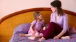 Mother sits on bed with daughter and tells about something