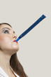 Close-up of a young woman blowing blue party blower against gray background