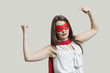 Photo: Portrait of a young woman in super hero costume flexing muscles over gray background Portrait of a young woman in super hero costume flexing muscles over gray background