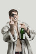 Photo: Portrait of young man with a rude gesture while holding beer bottle against gray background Portrait of young man with a rude gesture while holding beer bottle against gray background