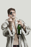 Photo: Portrait of young man with a rude gesture while holding beer bottle against gray background Portrait of young man with a rude gesture while holding beer bottle against gray background