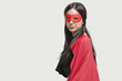 Portrait of young woman in superhero costume against gray background