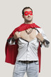 Young man in superhero costume standing against gray background