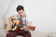 Young Caucasian man playing guitar while sitting on fur sofa