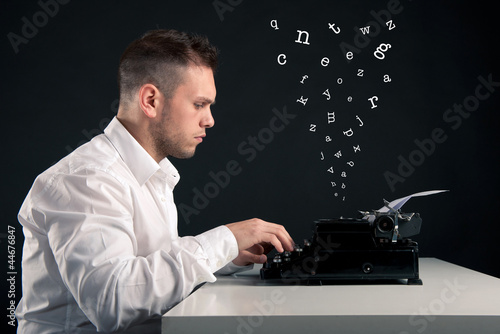 Photo: Young man writing with an old typewriter. Conceptual image Young man writing with an old typewriter. Conceptual image