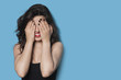 Cheerful young woman covering her face against blue background