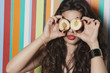 Young woman covering her eyes with peach against striped background