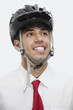 Photo: Young Indian businessman wearing cycling helmet while looking away against gray background Young Indian businessman wearing cycling helmet while looking away against gray background