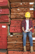 Photo: Asian female industrial worker using tablet PC while sitting on stacked wooden planks Asian female industrial worker using tablet PC while sitting on stacked wooden planks