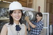 Photo: Portrait of woman smiling with female industrial worker carrying propane cylinder in background Portrait of woman smiling with female industrial worker carrying propane cylinder in background