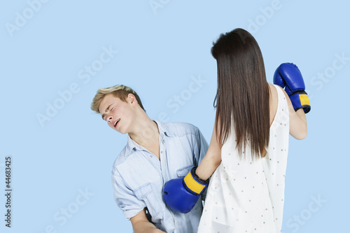 Photo: Young female boxer punching man over blue background Young female boxer punching man over blue background