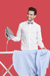 Happy man in formals ironing shirt over red background