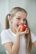 Portrait of happy young girl eating an apple over gray background