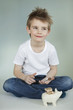 Thoughtful boy with piggy bank and coins over gray background