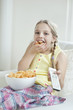 Girl watching TV as she stuffs her mouth with wheel shape snack pellets