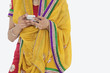 Photo: Midsection of woman in Indian clothing using cell phone over white background Midsection of woman in Indian clothing using cell phone over white background