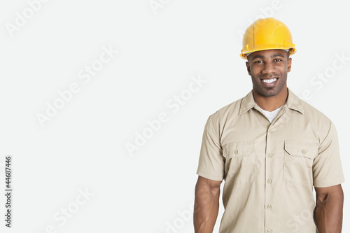 Photo: Portrait of happy young African man wearing yellow hard hat helmet over gray background Portrait of happy young African man wearing yellow hard hat helmet over gray background