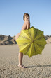 Portrait of a happy naked woman with yellow umbrella on barren landscape