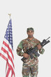 Foto: Portrait of US Marine Corps soldier with M4 assault rifle standing by American flag over gray background Portrait of US Marine Corps soldier with M4 assault rifle standing by American flag over gray background