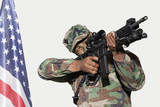 Photo: US Marine Corps soldier aiming M4 assault rifle with American flag against gray background US Marine Corps soldier aiming M4 assault rifle with American flag against gray background